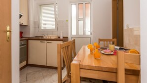 Une cuisine de taille réduite comprenant une table à manger, des chaises et une fenêtre avec des stores.