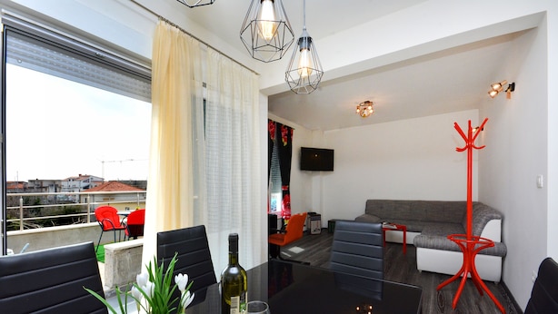 Una sala de estar moderna con un sofá, una mesa de comedor con sillas, una lámpara de pie roja y un televisor instalado en la pared.