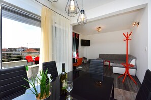 A modern living room with a sofa, a dining table with chairs, a red floor lamp, and a TV mounted on the wall. - Luxury Apartment Mio (Podstrana)