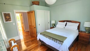 A bedroom with a bed, wooden nightstands, two wall-mounted lamps, a door, and a window with curtains. - Rewa House ~ city home, 3 bedrooms, walk to CBD (Christchurch)