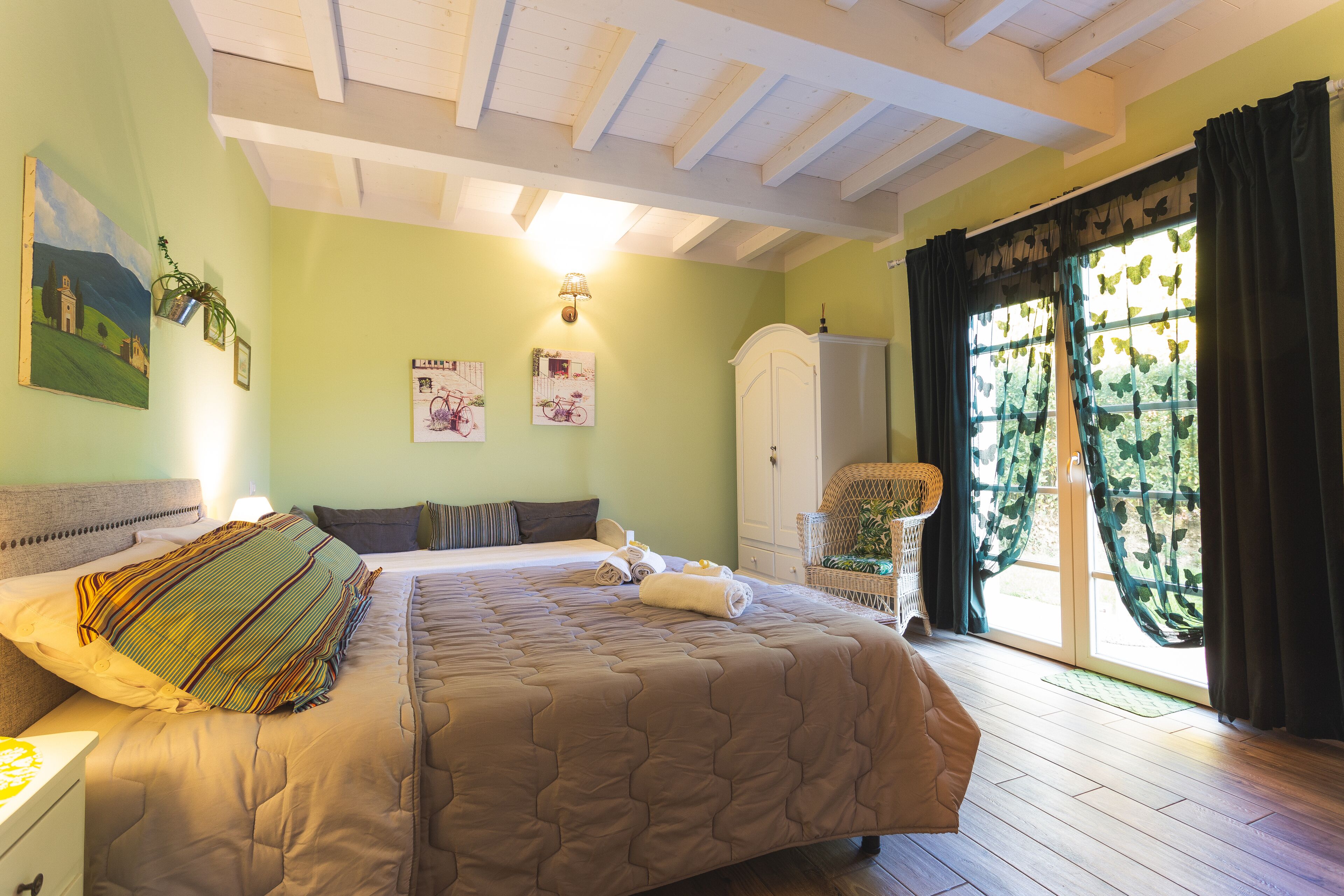 Un dormitorio con una cama grande, un armario, una silla y un ventanal con cortinas.