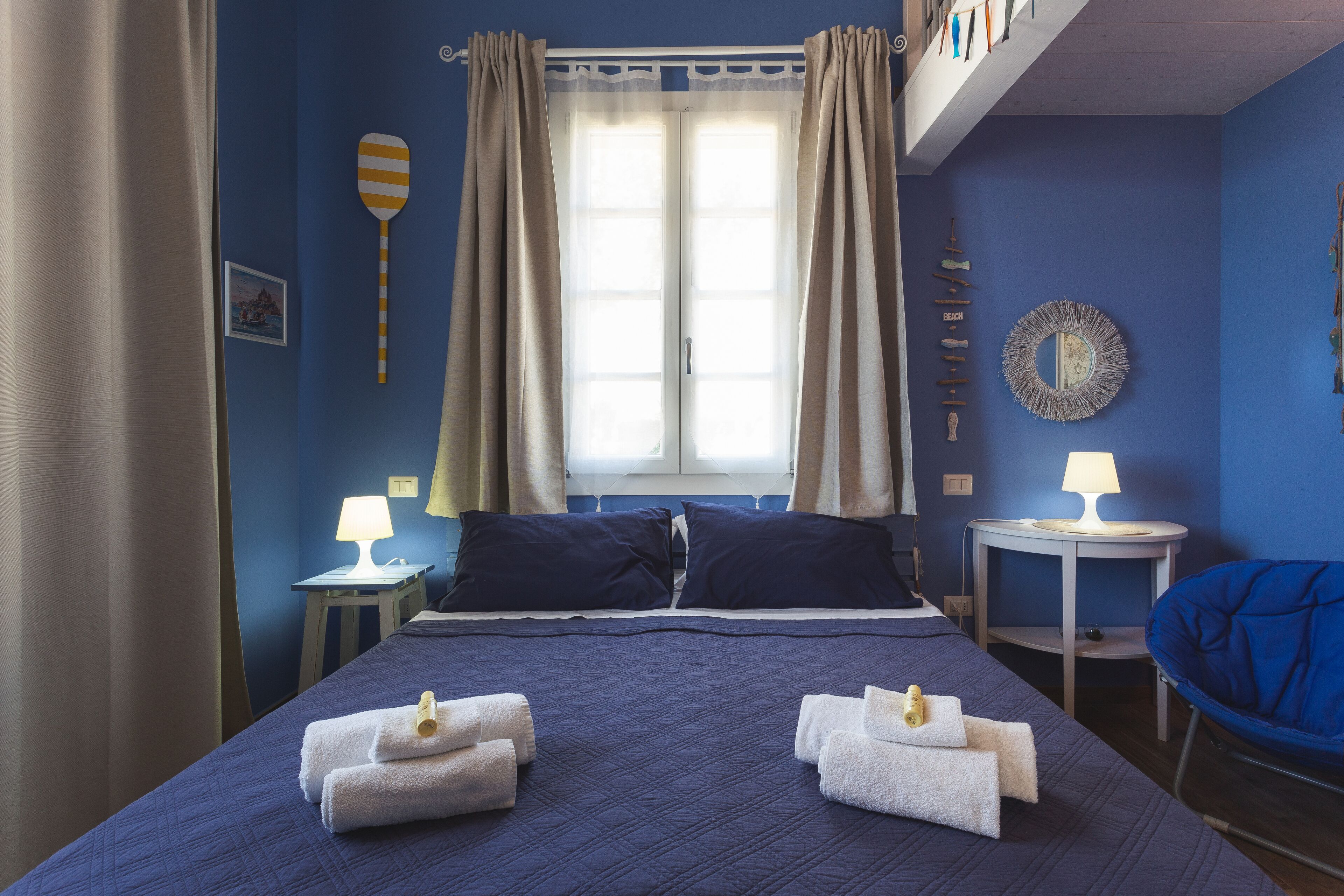 Habitación de hotel con una cama grande, dos mesitas de noche con lámparas, una silla y una ventana con cortinas.