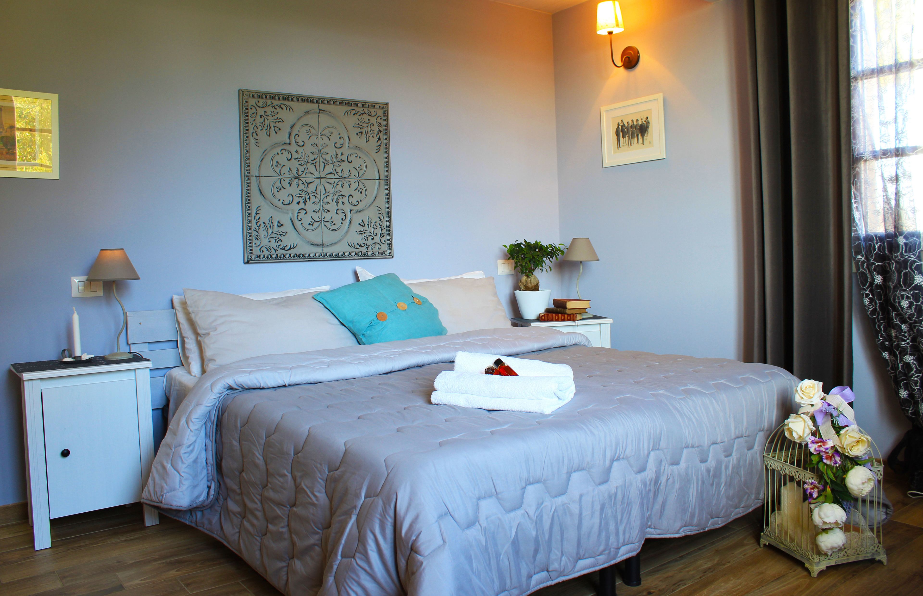 A neatly arranged bedroom with a large bed, two bedside tables, a wall-mounted lamp, and a decorative wall piece.