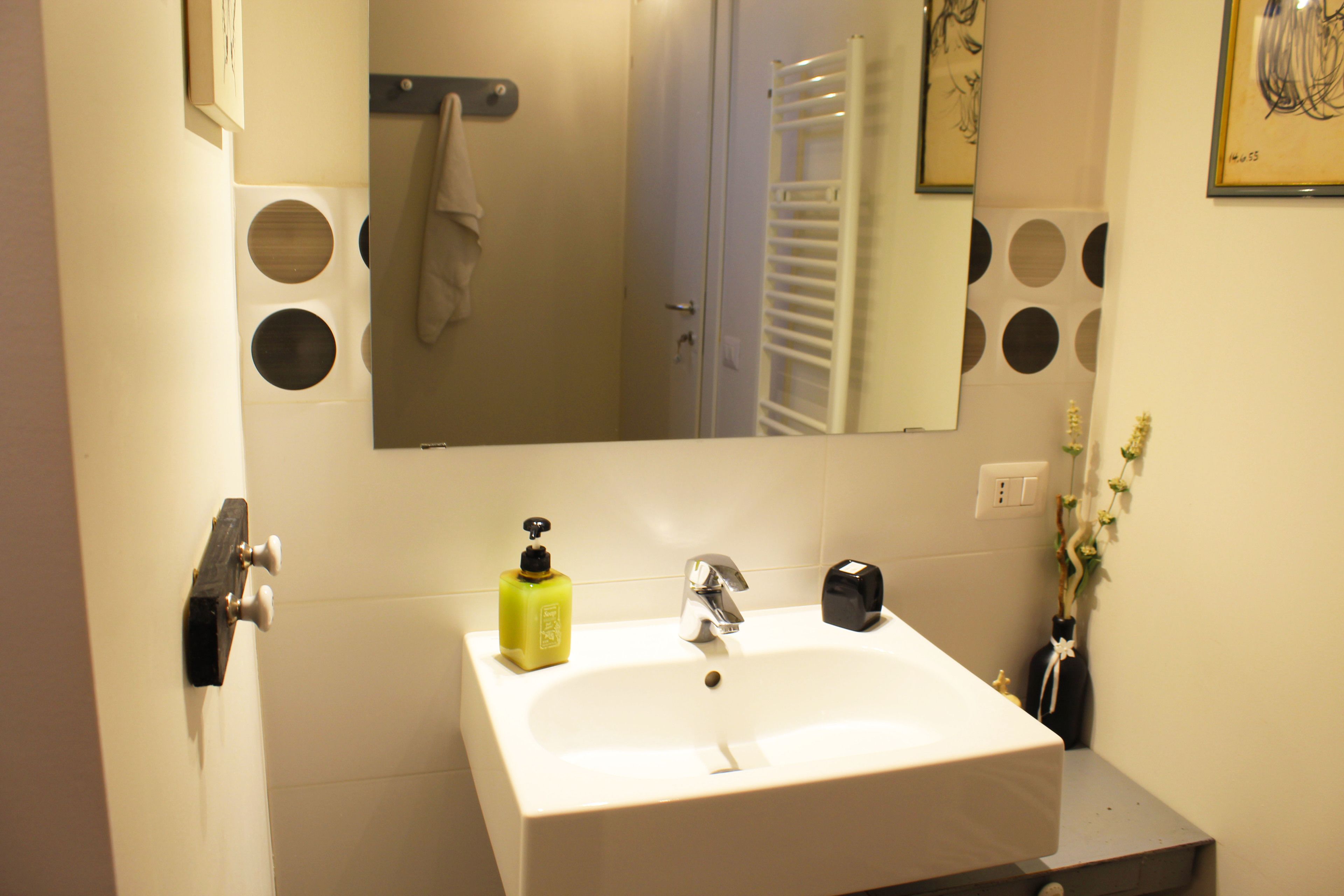 Un bagno con lavandino bianco, uno specchio, un portascopevoli e un water.