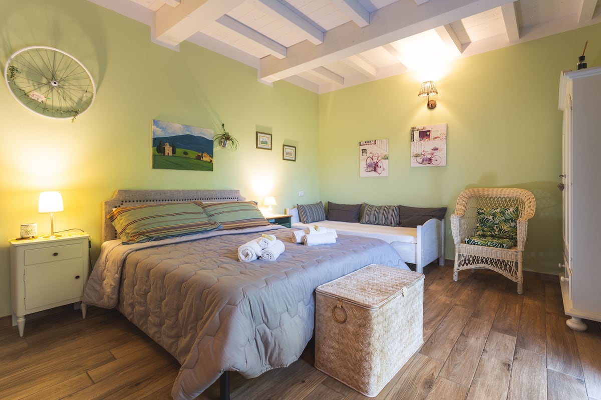 Un dormitorio con cama, mesita de noche, lámpara y una silla de mimbre.
