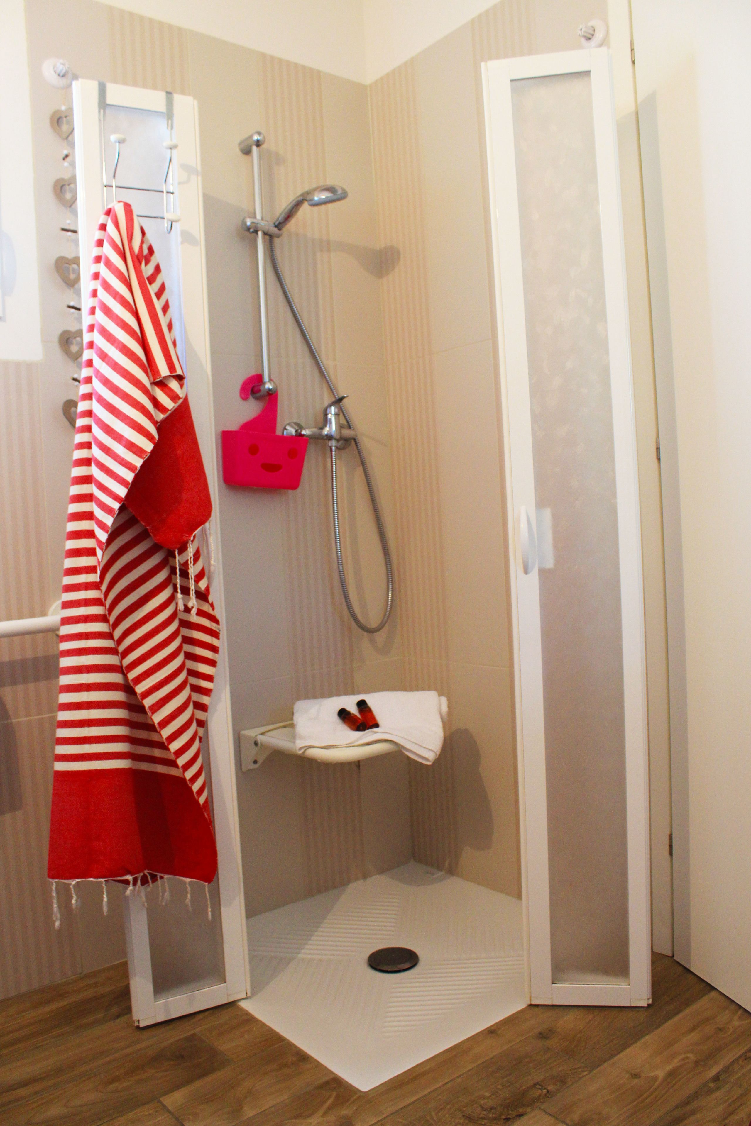 Un espace douche avec une porte blanche, une serviette rayée rouge et blanche, et une petite étagère sur laquelle est posée une serviette blanche.