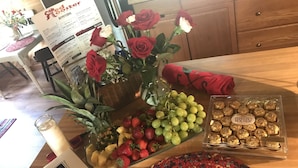 Une table avec un menu, un bouquet de roses, un assortiment de fruits, des chocolats Ferrero Rocher et un set de table en fibres tressées.