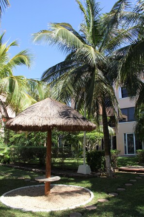 Relax in a serene garden setting surrounded by lush greenery and a charming thatched-roof gazebo.
