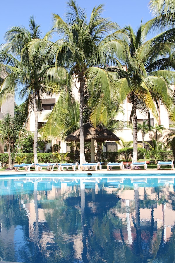 Relax by the pool surrounded by palm trees and a multi-story building with balconies.