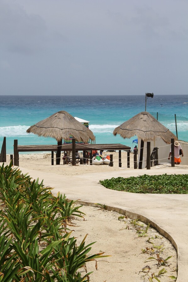 Una playa con sombrillas de paja, una estructura de madera y vistas al océano.