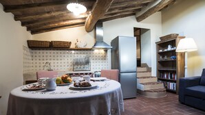 A cozy kitchen with a dining table set for two, a refrigerator, and a bookshelf. - Small Apartment With Independent Access  In Beautiful Tuscan Farmhouse (Castelnuovo Berardenga)