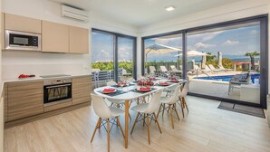 Una cucina moderna con zona pranzo che si affaccia su una piscina e montagne.