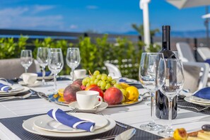 A table set for a meal with plates, glasses, and a bottle of wine, with a fruit platter in the background. - JAZZ at Rova Villa Luna (Malinska-Dubasnica)