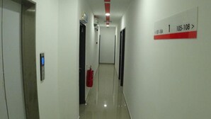 Un pasillo largo y estrecho con paredes blancas y techo rojo. Se observa un extintor de incendios en la pared, además de un cartel con números de habitación.