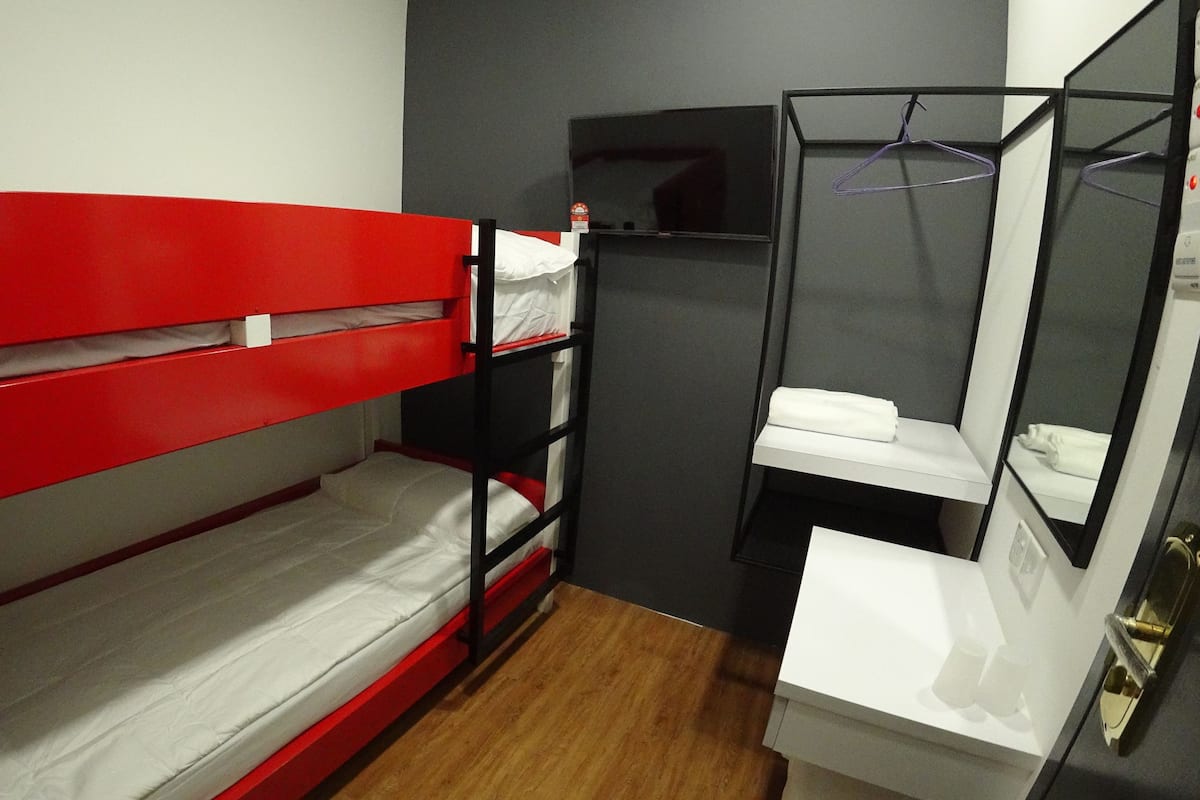 A bunk bed with red headboard, a white sink, and a mirror in a small room with wooden flooring.