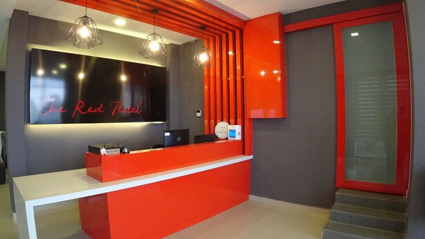 Un mostrador de recepción con una decoración en rojo y negro, un reloj digital y un letrero que dice "The Red Hotel".
