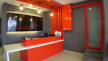 Un mostrador de recepción con una decoración en rojo y negro, un reloj digital y un letrero que dice "The Red Hotel".