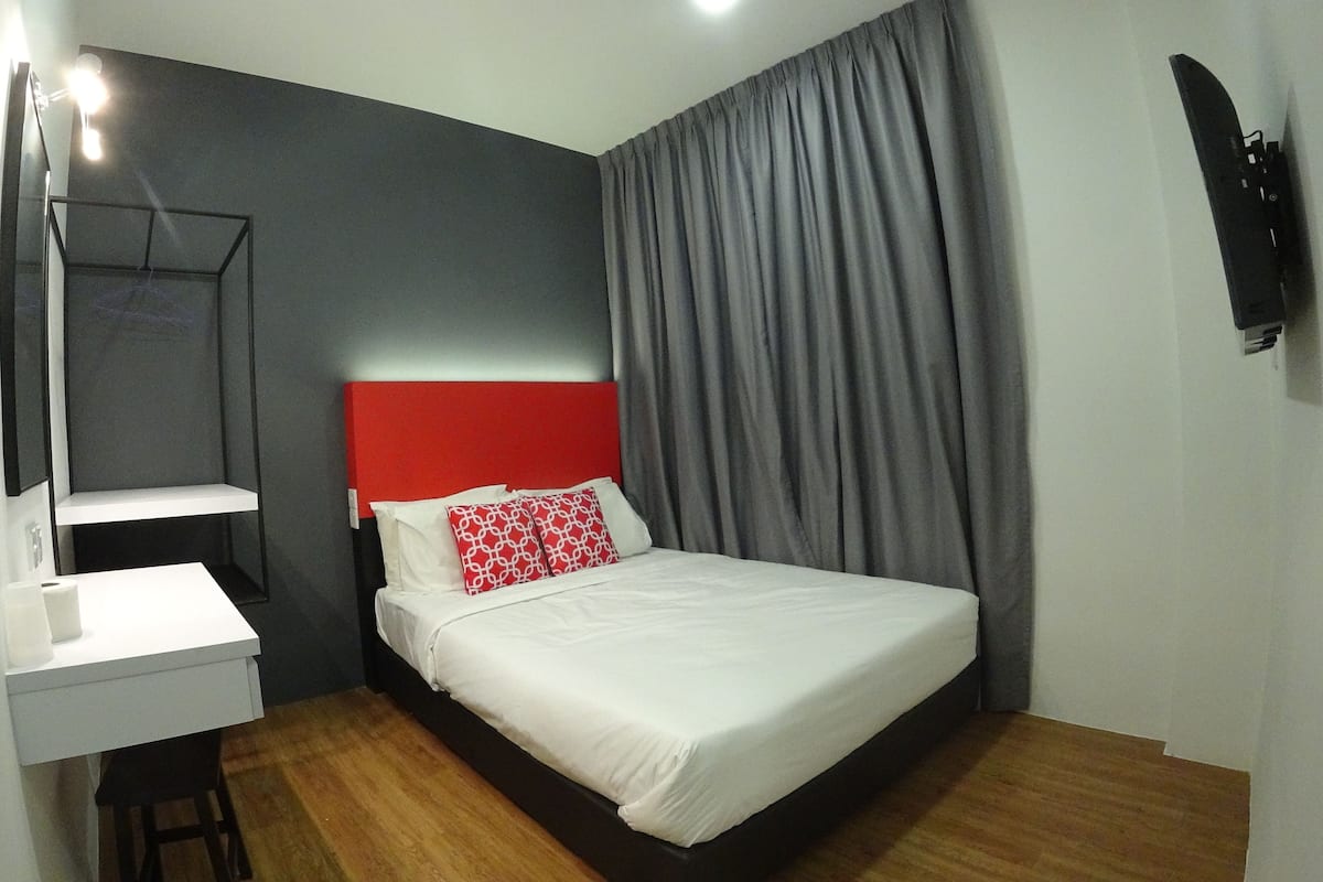 A bedroom with a bed, a desk, a mirror, and a wall-mounted TV.