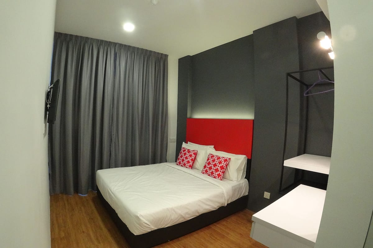 A modern bedroom with a bed, grey curtains, a red headboard, and a white bedside table.