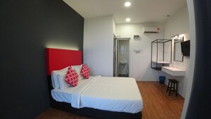 Habitación de hotel con cama, cabecera roja, colchón blanco, piso de madera, baño con lavamanos y espejo, y unidad de aire acondicionado.