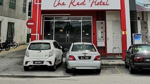 Un hotel con fachada moderna, que destaca un cartel grande con la palabra 'HOTEL' en la parte superior y la señalización 'The Red Hotel' debajo.