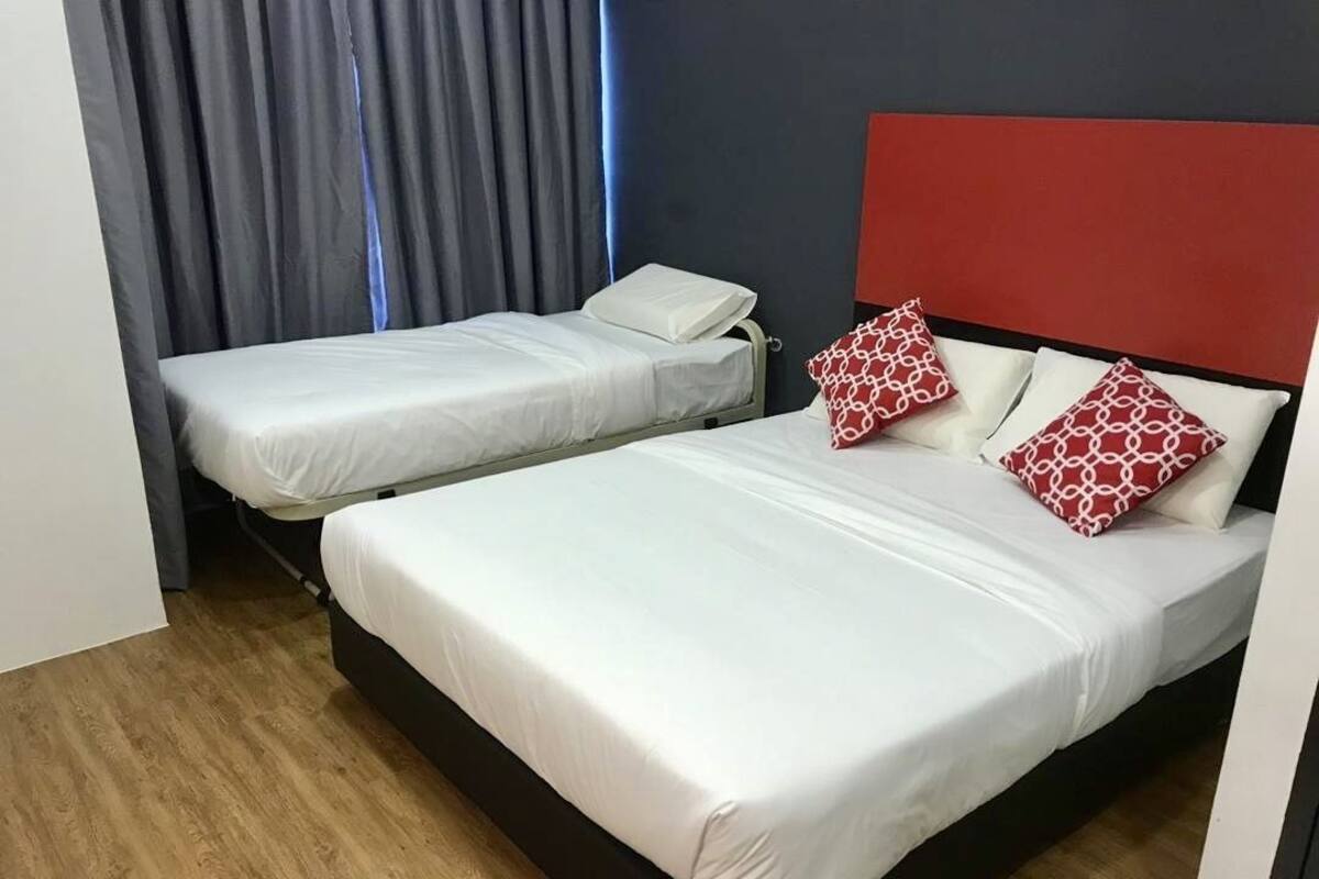 A hotel room with two beds, a red headboard, and a grey curtain.