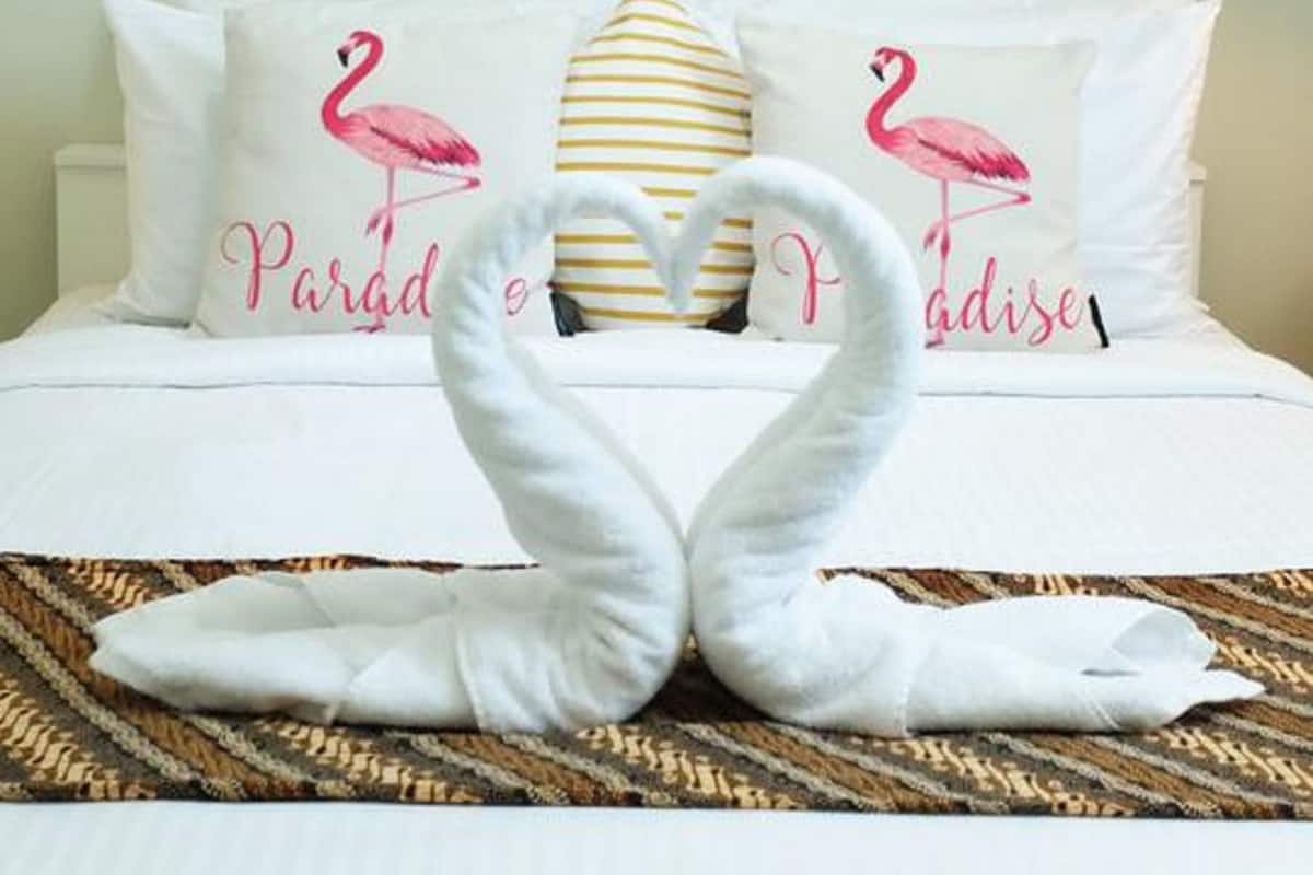 A hotel room with a bed, two pillows with flamingo designs, and two framed flamingo paintings on the wall.