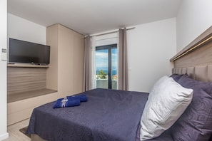 A modern bedroom with a large bed, a flat-screen TV mounted on the wall, and a balcony with a city view. - JAZZ at Rova Villa Sola (Malinska-Dubasnica)