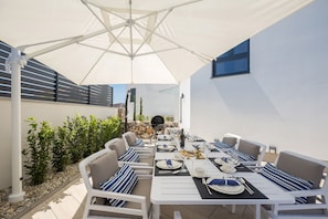 An outdoor dining area with white tables and chairs, a large umbrella, and a stone wall in the background. - JAZZ at Rova Villa Sola (Malinska-Dubasnica)