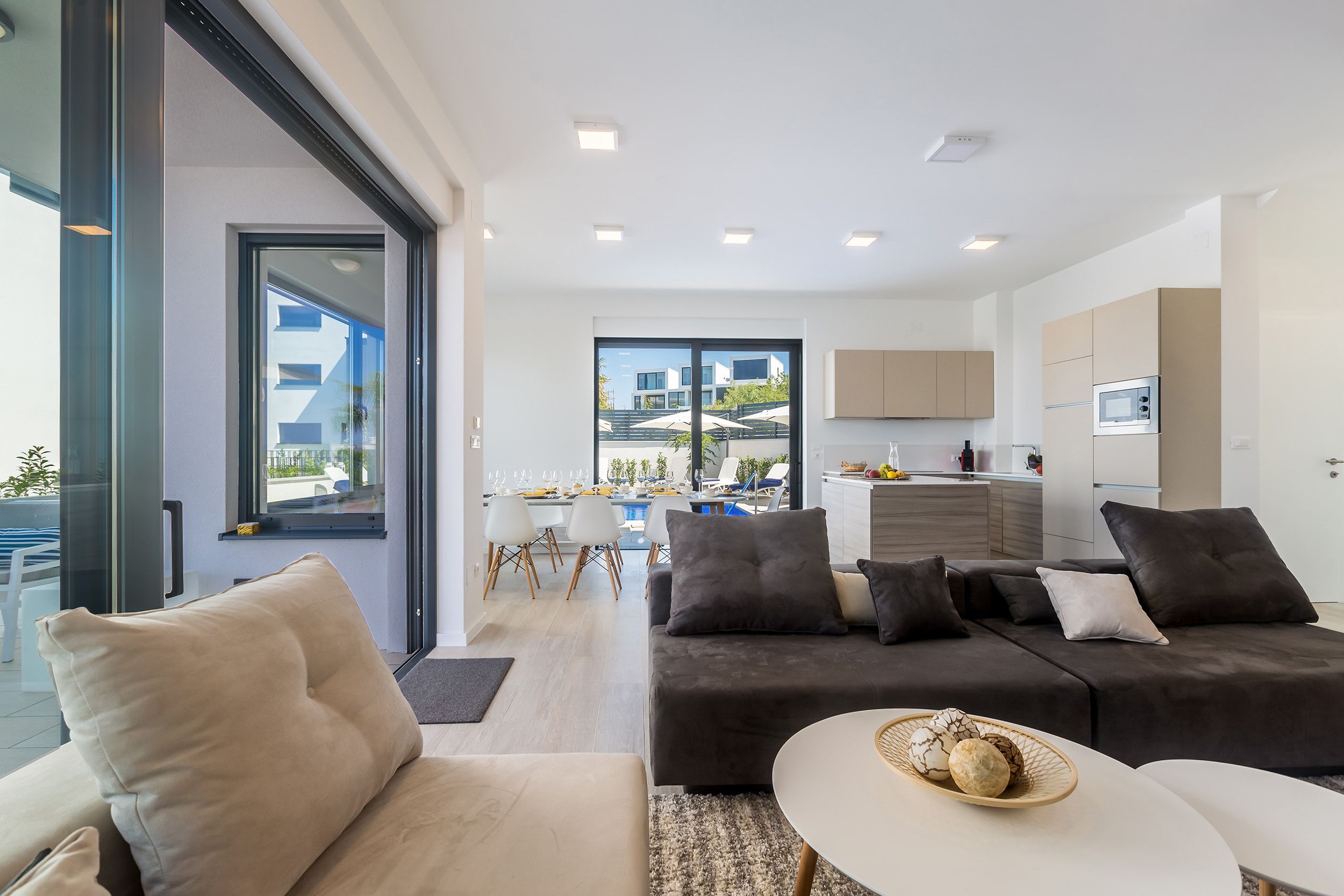 A modern living room with a sofa, a dining area with a table and chairs, and a kitchen area with cabinets and appliances.