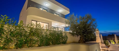 Ein modernes, zweistöckiges Haus mit Balkon, Sitzgelegenheit im Freien und einem gut beleuchteten Garten.