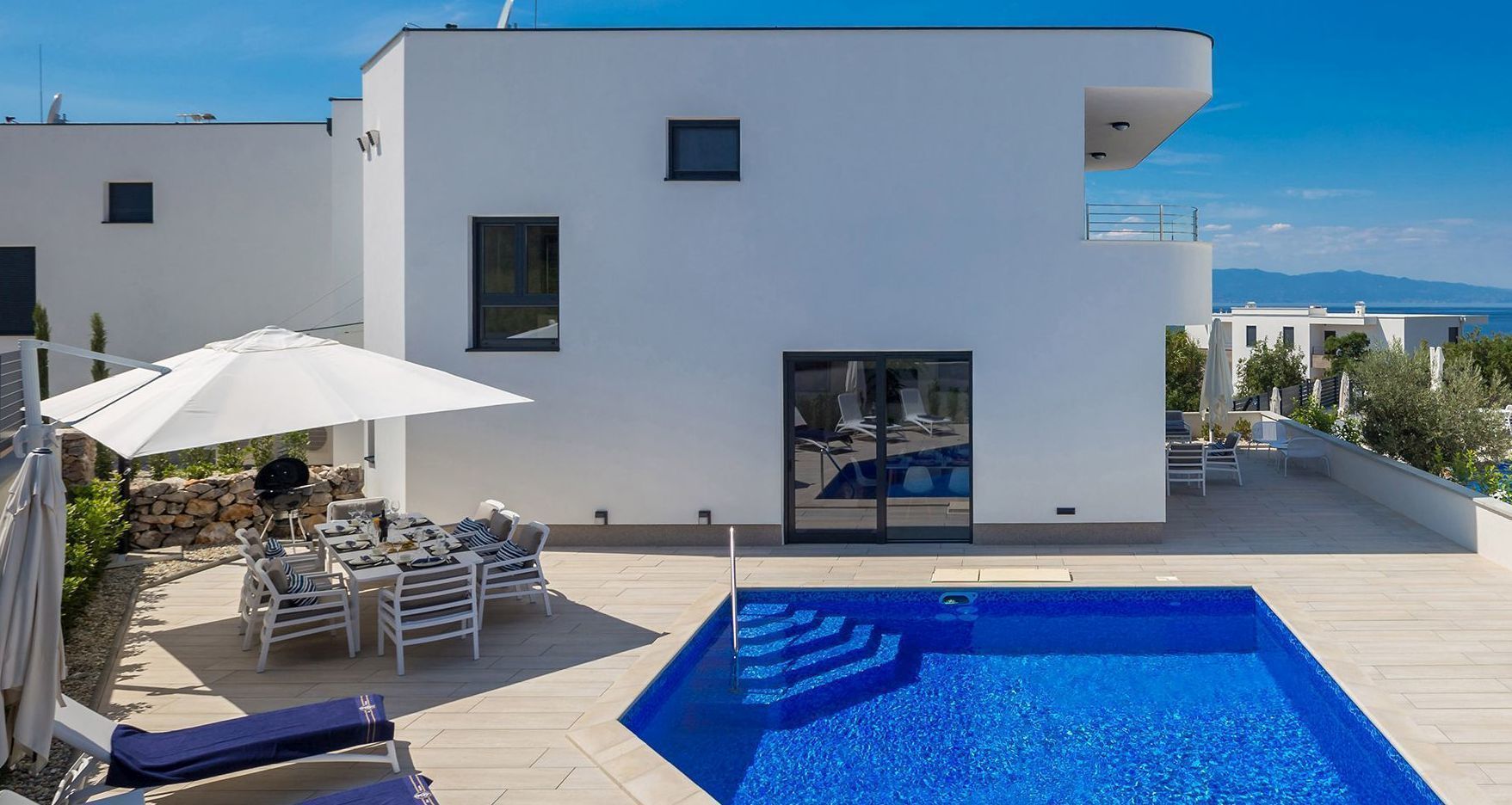 A modern house with a swimming pool, outdoor seating, and a view of the sea.
