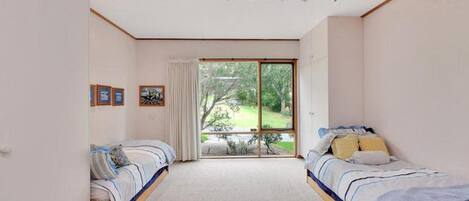 Ein Schlafzimmer mit zwei Betten, einer großen Schiebetür zu einem Garten und einer Decke mit Einbauleuchten.