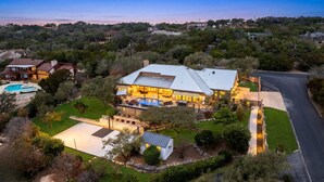 A large house with a swimming pool, tennis court, and a well-maintained lawn. - Experience Vista Grande: 4600 sq ft. of Luxury - Heatable Pool and City Views (Helotes)