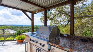 An outdoor barbecue area with a grill, a potted plant, and a view of the landscape. - Experience Vista Grande: 4600 sq ft. of Luxury - Heatable Pool and City Views (Helotes)