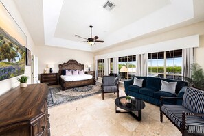 A spacious living room with a large bed, a blue sofa set, a coffee table, and a view of the outdoors through large windows.