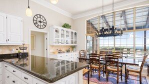A spacious kitchen with white cabinetry, a granite countertop, and a dining area with wooden chairs and a table. - Experience Vista Grande: 4600 sq ft. of Luxury - Heatable Pool and City Views (Helotes)