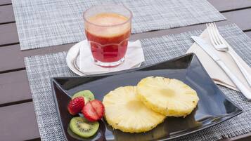 Comida con un vaso de jugo, rodajas de piña y kiwi en un plato, sobre una mesa con posavasos.