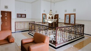 Una habitación amplia con candelabro, puerta de madera y balcón con barandilla decorativa.