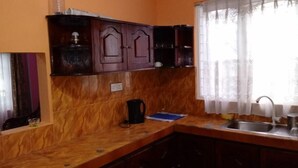 Una cocina con armarios de madera, un lavamanos y un ventanal con cortinas ligeras.
