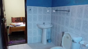 Baño con inodoro, lavamanos y una cama visible a través de una puerta abierta.