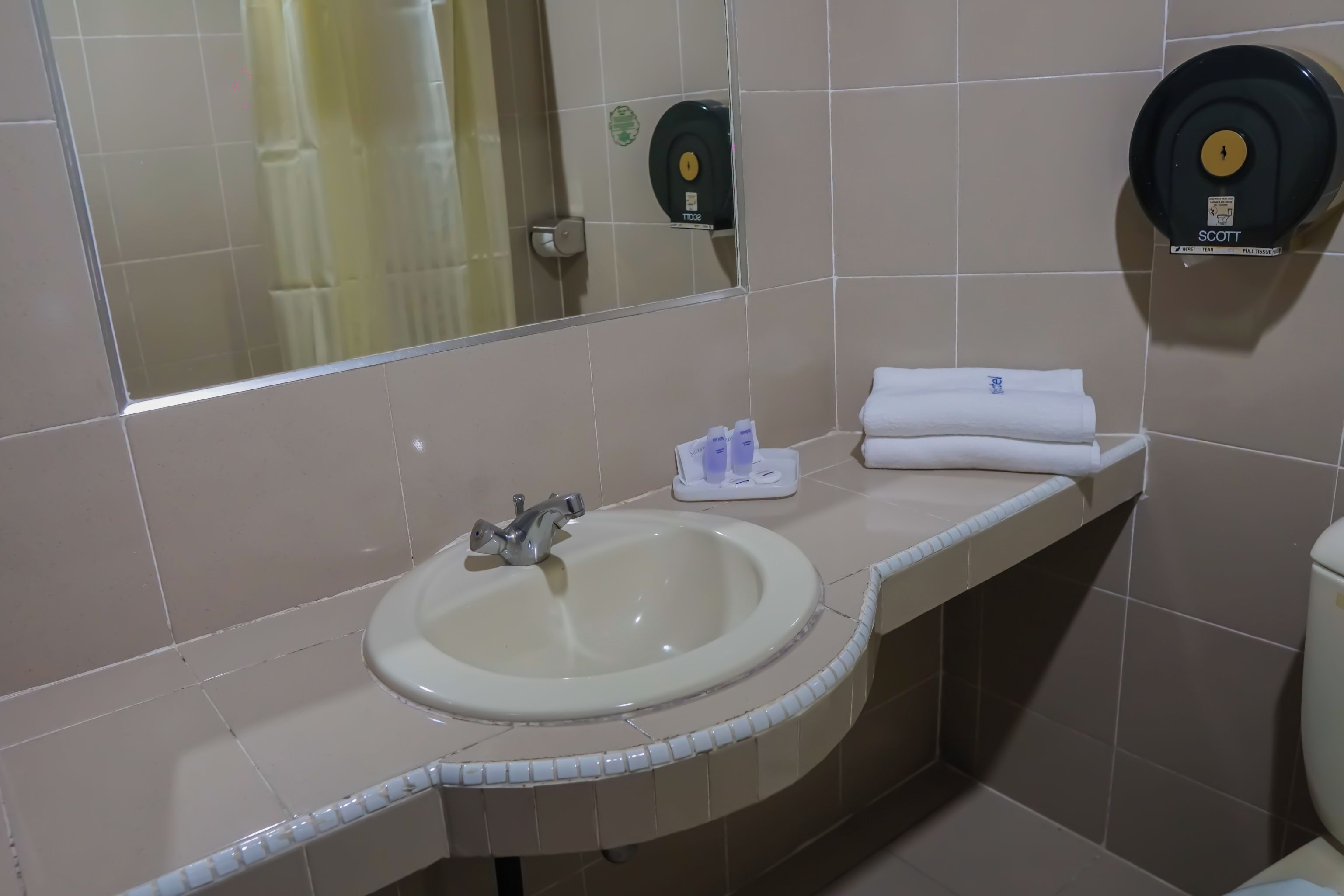 Baño con lavamanos, espejo, dispensador de toallas y retrete.