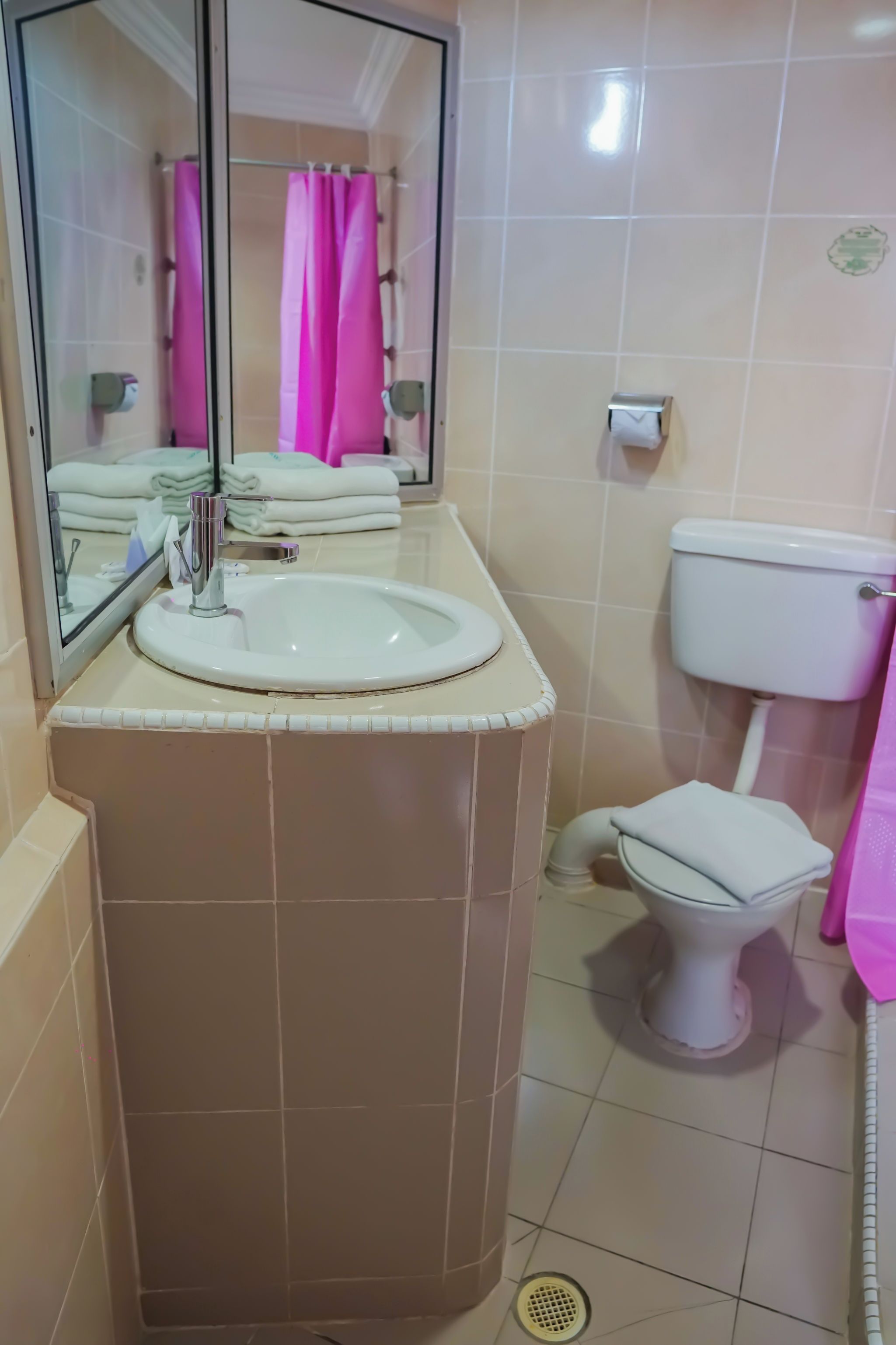 A bathroom with a sink, mirror, toilet, and pink towels.