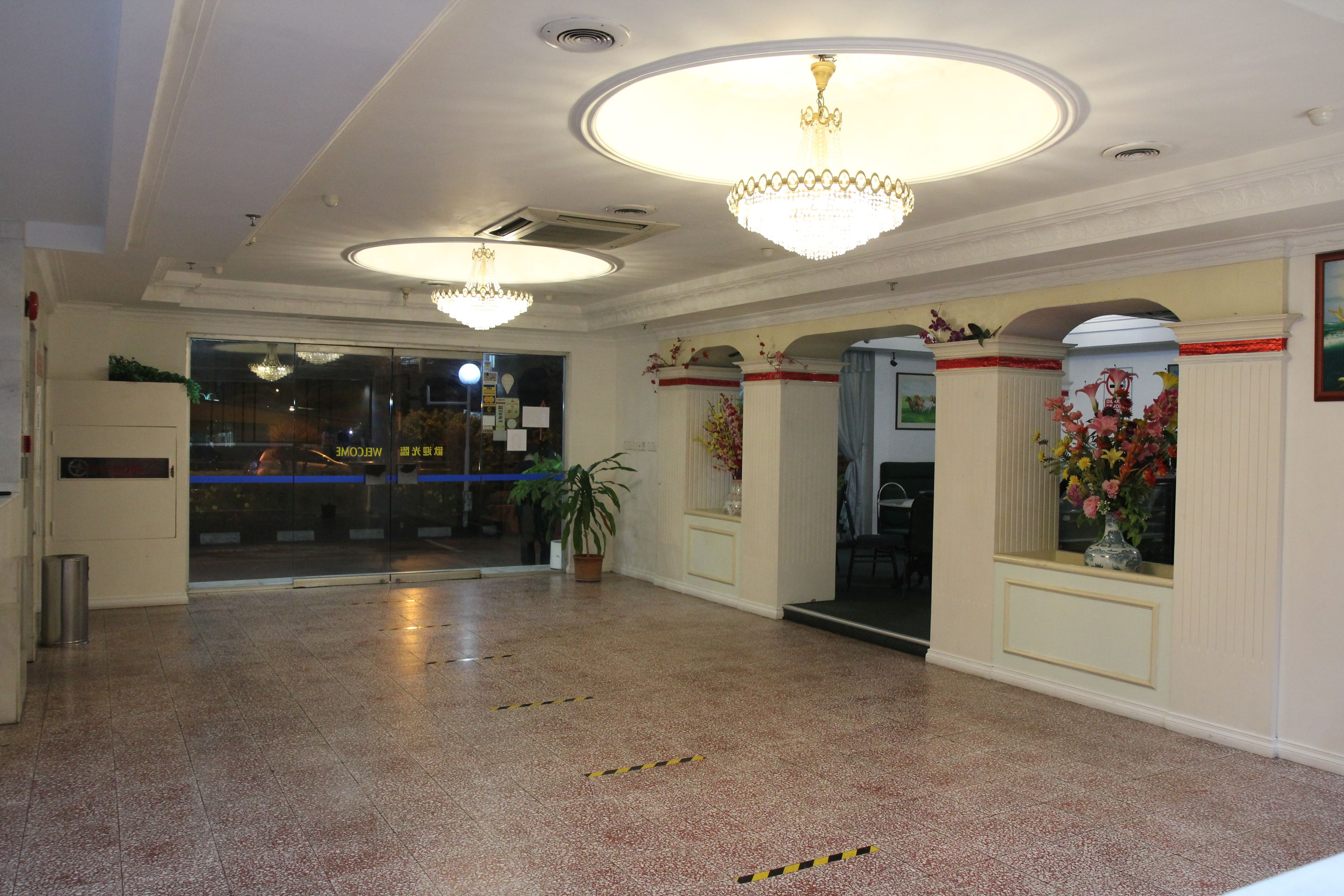 A spacious lobby with a high ceiling, chandeliers, a reception desk, and a potted plant.