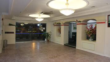 A spacious lobby with a high ceiling, chandeliers, a reception desk, and a potted plant.