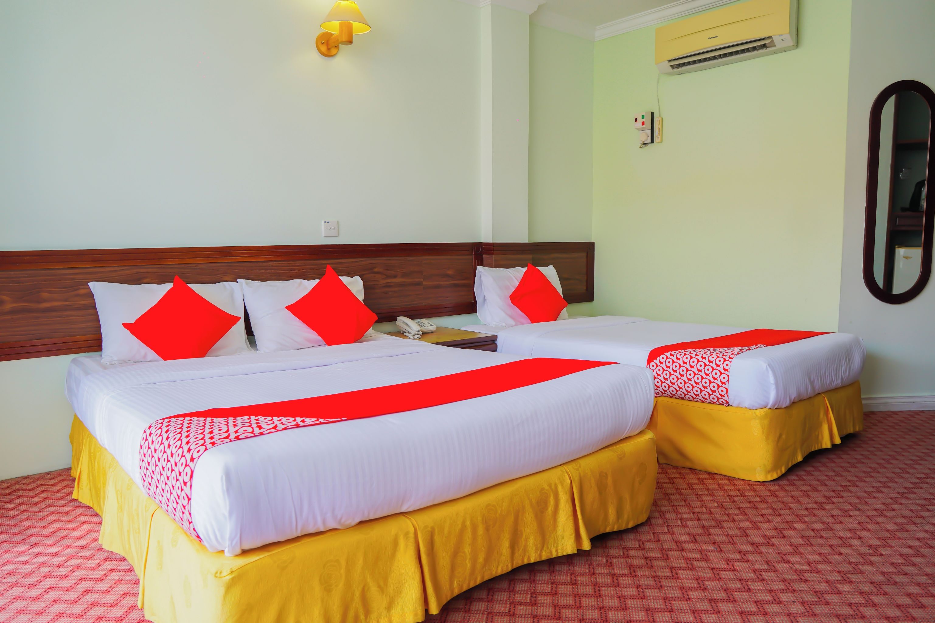 Une chambre d’hôtel avec deux lits, chacun agrémenté de draps blancs et de touches de couleur rouge, un téléphone sur la table de chevet et un climatiseur fixé au mur.