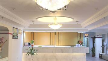A spacious lobby with a marble reception desk, a large chandelier, and potted plants.
