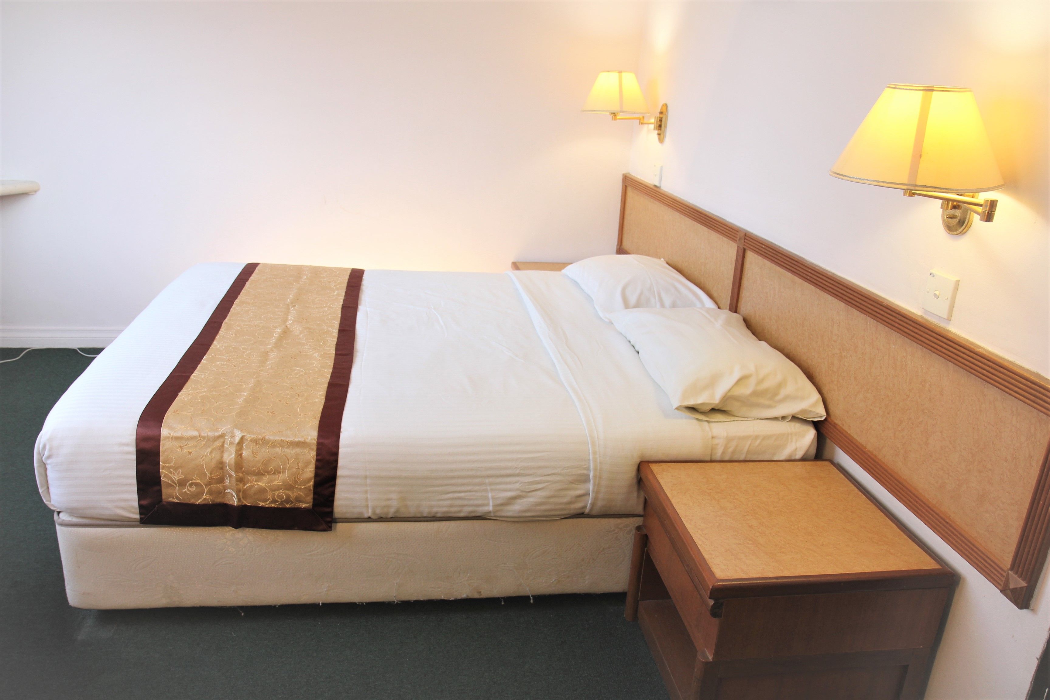 A hotel room with a bed, bedside tables, and wall-mounted lamps.