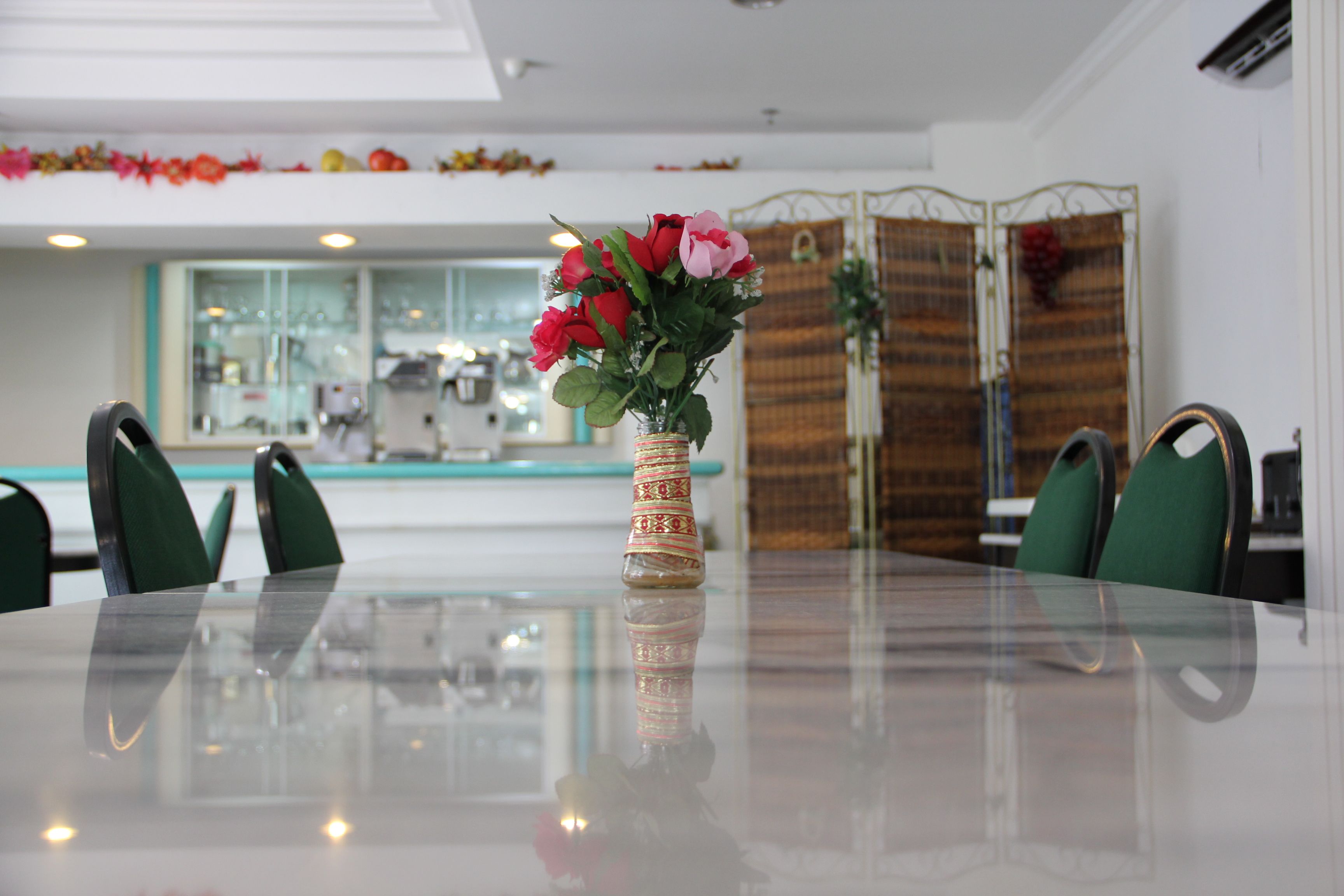 A dining table with a vase of flowers, green chairs, and a glass-top table in a modern interior with a kitchen in the background.