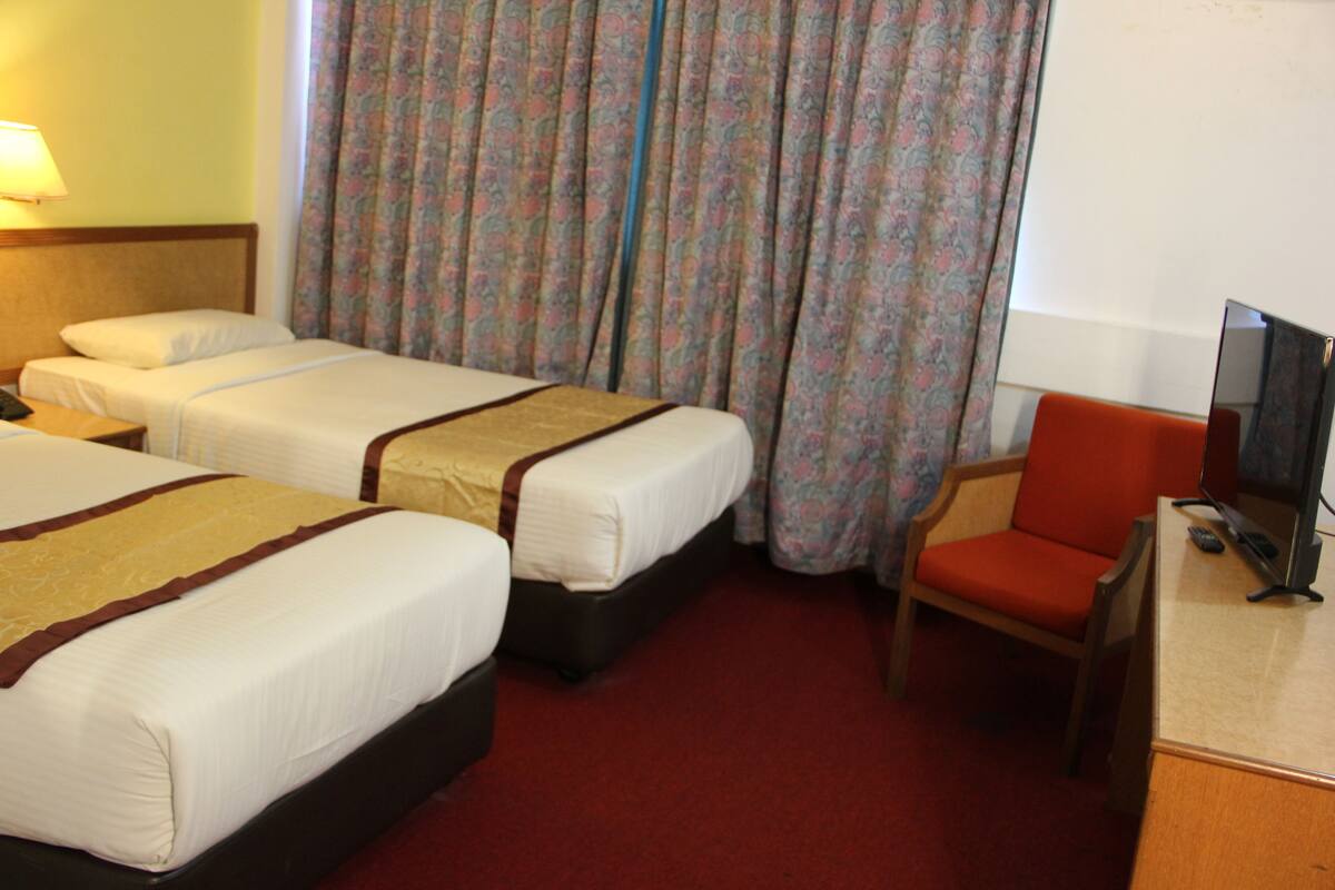 Habitación de hotel con dos camas, alfombra roja, televisión y una silla.